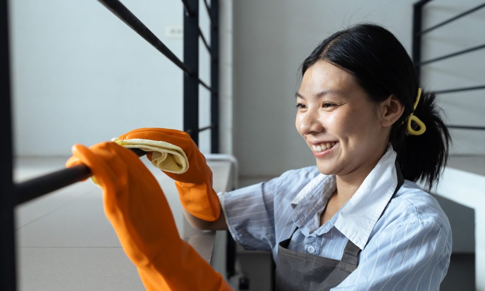 Hands in blue rubber gloves holding microfiber cleaning cloth make cleaning and disinfection for good hygiene of a stair railing.